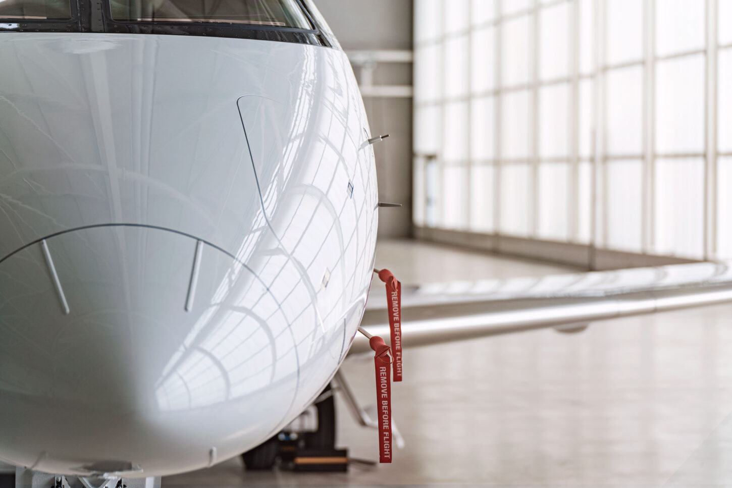 close up on the nose of a parked aircraft inside the hangar with two red safety ribbons hangig from it saying 